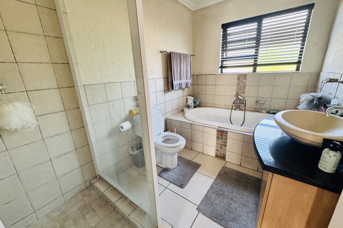 A functional bathroom featuring a glass-enclosed shower, built-in bathtub, toilet, and a vanity basin with a granite countertop.
