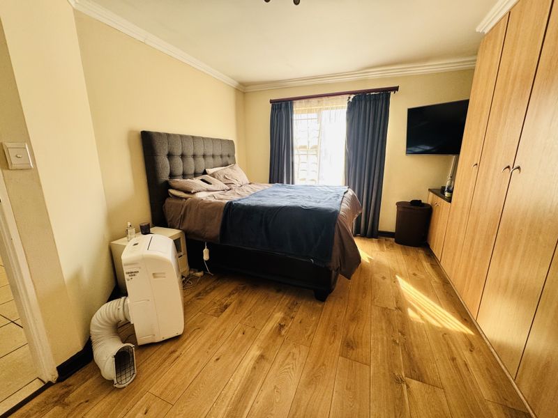 A functional bedroom featuring laminate flooring, built-in wooden cupboards, and decorative ceiling cornicing, providing a practical and comfortable living space.