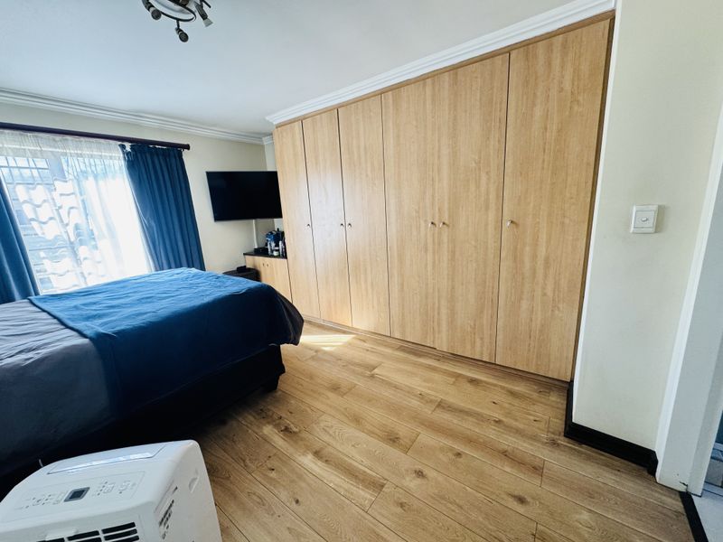 A well-maintained bedroom featuring extensive built-in wooden cupboards, modern laminate flooring, and classic ceiling cornice detailing.