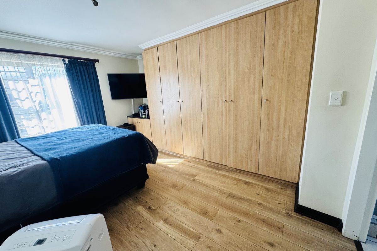 A well-maintained bedroom featuring extensive built-in wooden cupboards, modern laminate flooring, and classic ceiling cornice detailing.