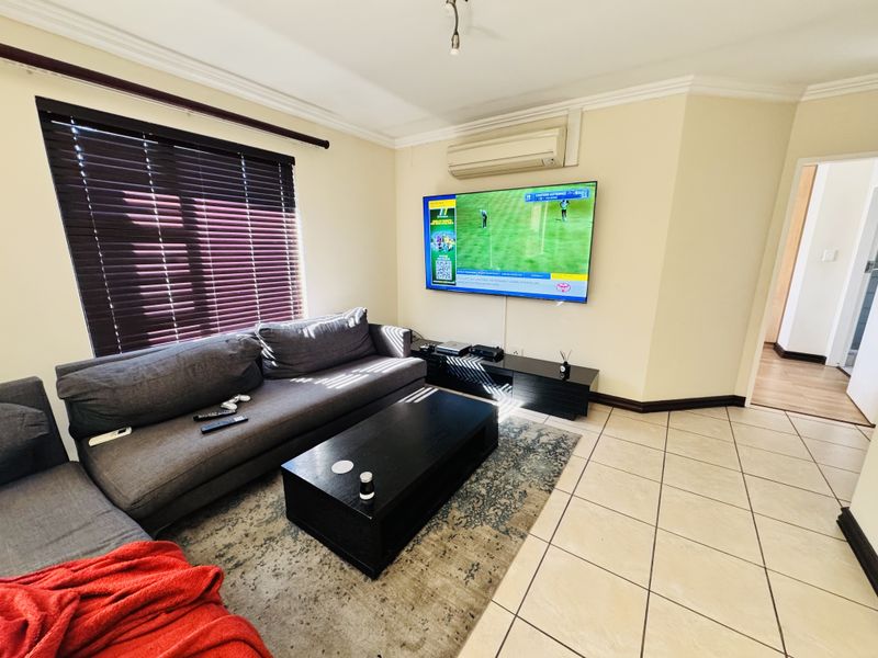 A living room featuring tiled flooring, coving, venetian blinds, and a wall-mounted air conditioning unit.