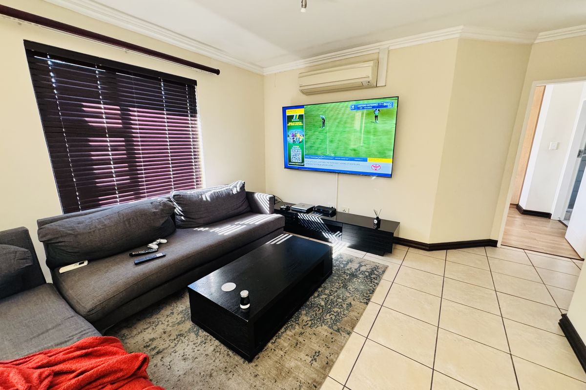 A living room featuring tiled flooring, coving, venetian blinds, and a wall-mounted air conditioning unit.