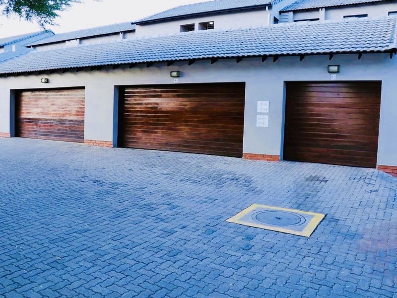 A row of modern garages with wooden sectional doors and a paved driveway in a well-maintained residential complex.