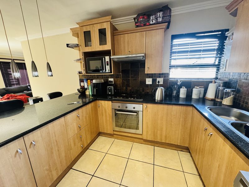 A functional kitchen featuring light wood cabinetry, granite countertops, a built-in oven with hob, and tiled flooring with a breakfast bar area.
