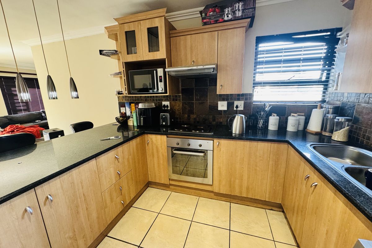 A functional kitchen featuring light wood cabinetry, granite countertops, a built-in oven with hob, and tiled flooring with a breakfast bar area.