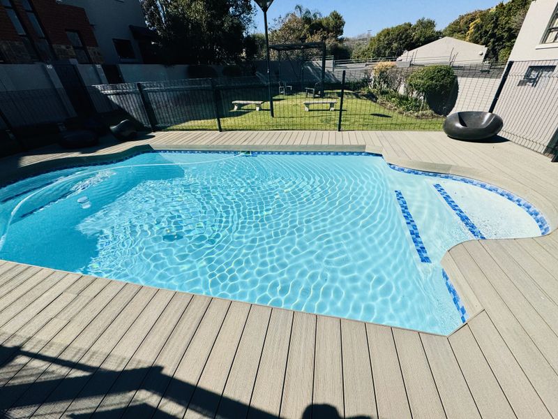 A well-maintained swimming pool area featuring composite decking, perimeter fencing, and a landscaped lawn.