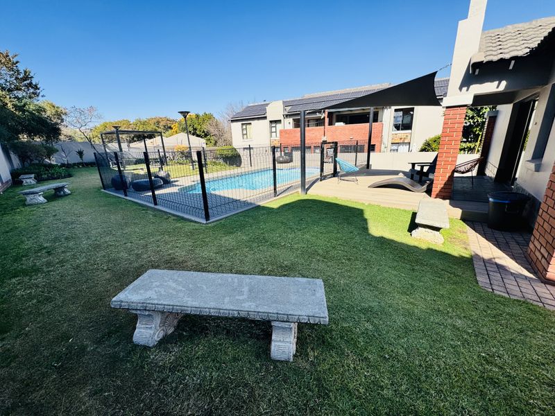 A well-maintained outdoor area featuring a swimming pool with safety fencing, wooden decking, and a landscaped garden with brick architectural elements.