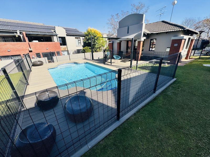A well-maintained outdoor pool area featuring composite decking, secure pool fencing, and a landscaped garden setting.