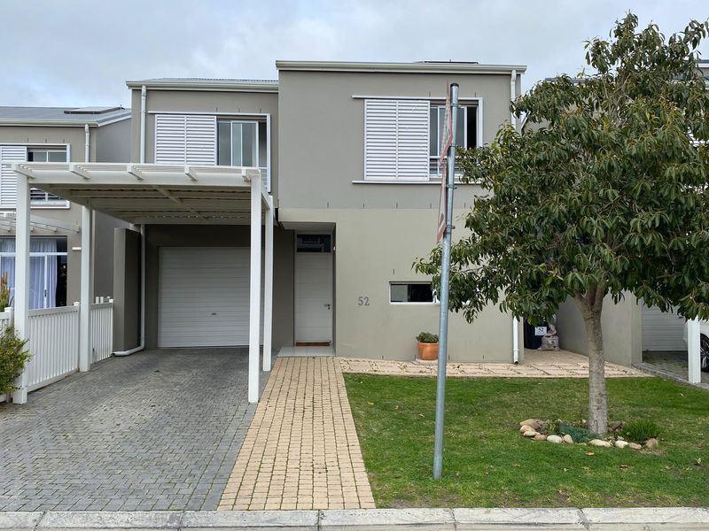 Front elevation of a modern two-story townhouse featuring a paved driveway, covered carport, and a neat front garden with a paved walkway.
