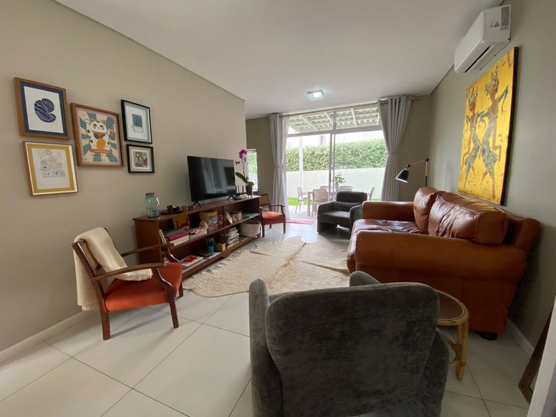 A comfortable living room featuring tiled flooring, a wall-mounted air conditioning unit, and large sliding glass doors that provide access to the outdoor patio area.