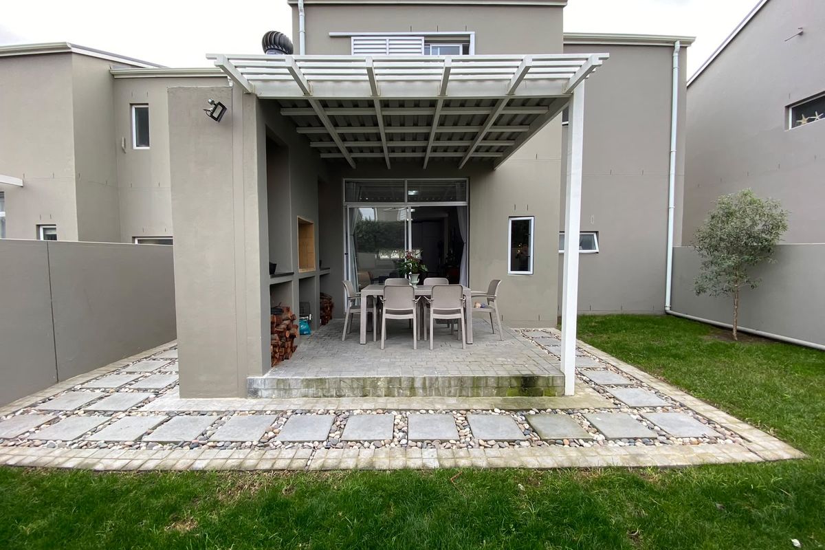 Rear view of the property featuring a covered patio with a built-in braai, paved flooring, and access to the interior via sliding glass doors.