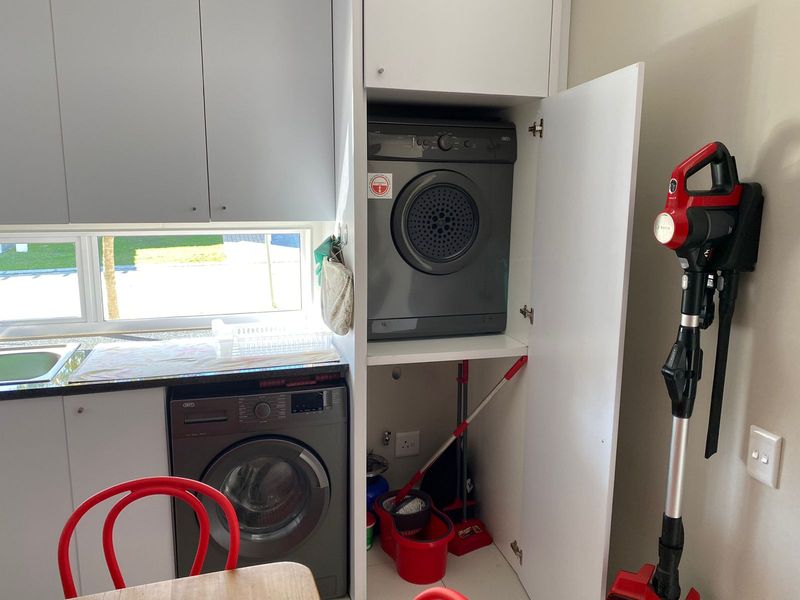 A functional laundry area featuring built-in cabinetry, integrated washing machine and tumble dryer, and a convenient sink with countertop space.