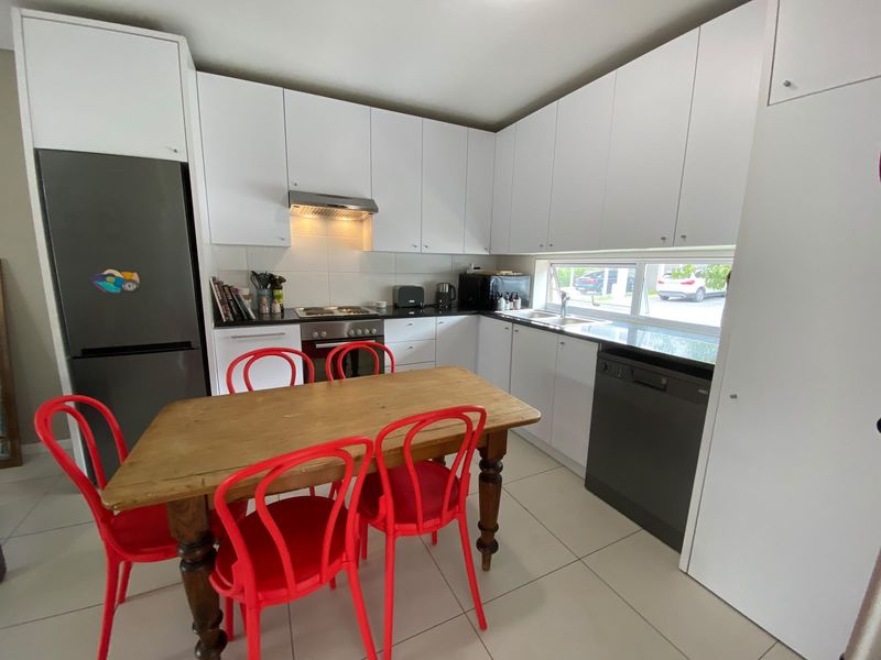 A functional kitchen featuring white cabinetry, dark countertops, built-in appliances, and tiled flooring, with a window providing natural light.
