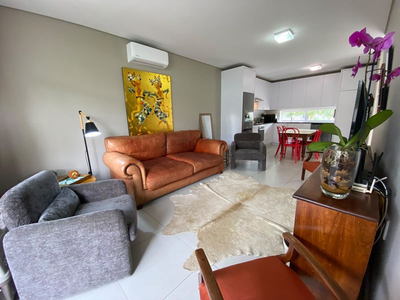 An open-plan living and kitchen area featuring modern white cabinetry, tiled flooring, and a wall-mounted air conditioning unit.