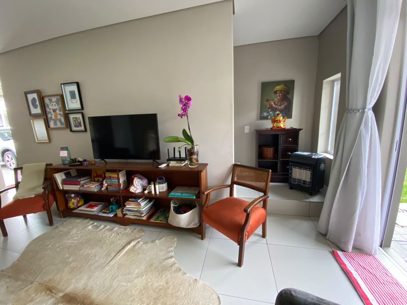 A bright living room featuring neutral wall tones, large format floor tiles, and a raised platform area near the window.