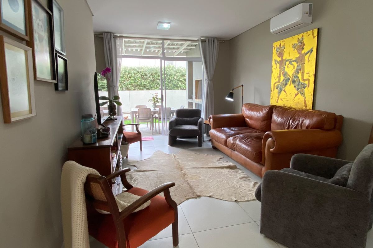 A well-maintained living room featuring tiled flooring, a wall-mounted split-system air conditioner, and large sliding glass doors providing access to the outdoor patio area.