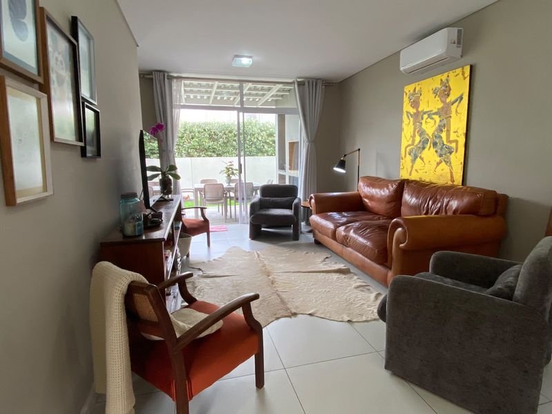 A well-maintained living room featuring tiled flooring, a wall-mounted split-system air conditioner, and large sliding glass doors providing access to the outdoor patio area.