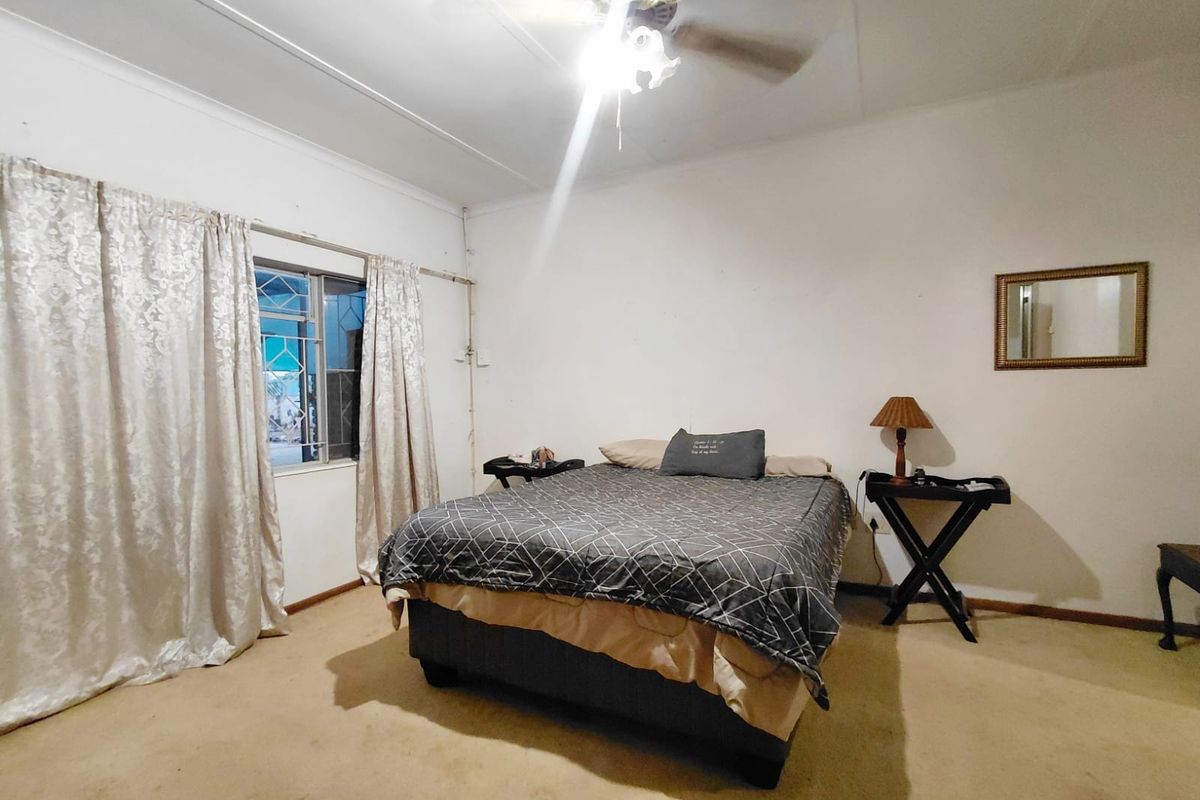 A bedroom featuring a ceiling fan, security bars on the window, and carpeted flooring. The room requires cosmetic updates to improve its overall condition.