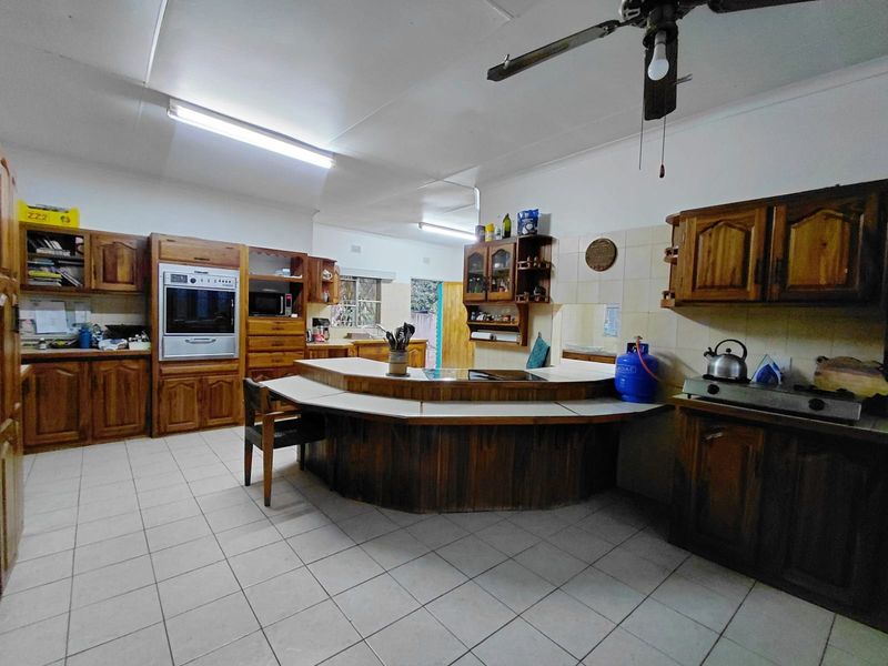 Spacious kitchen featuring extensive wooden cabinetry, a central island with integrated cooktop, built-in oven, and tiled flooring, offering significant potential for modern renovation.