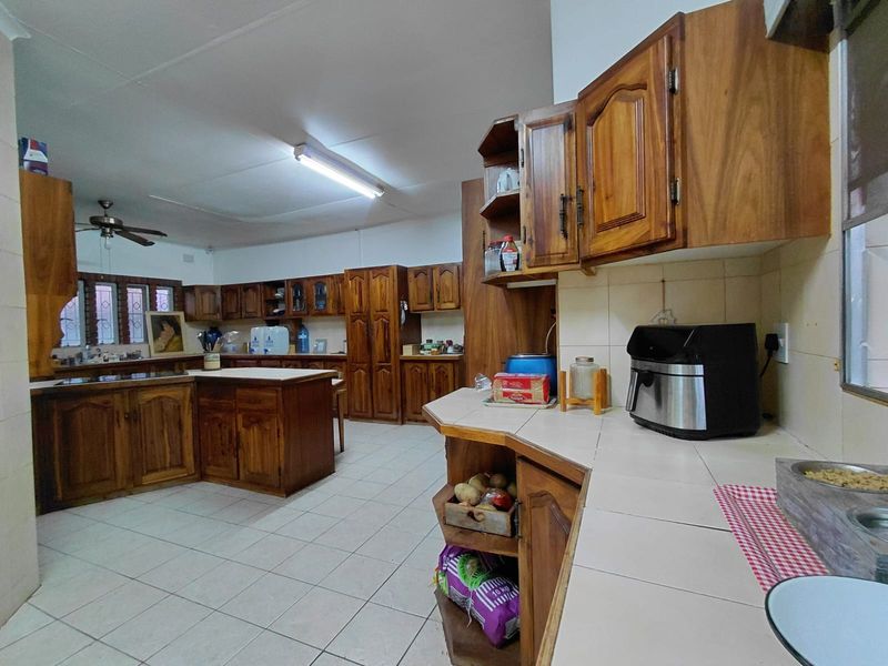Spacious kitchen featuring extensive wooden cabinetry, tiled countertops, and tiled flooring, offering a functional layout with ample storage space.