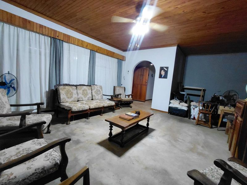 Spacious living area featuring a timber-clad ceiling, ceiling fan, and an arched doorway leading to an adjacent room, with unfinished concrete flooring throughout.