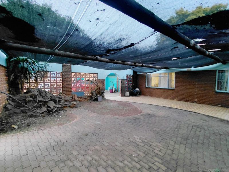 Outdoor patio area featuring brick paving, a decorative breeze block wall, and a large overhead shade cloth structure requiring maintenance.