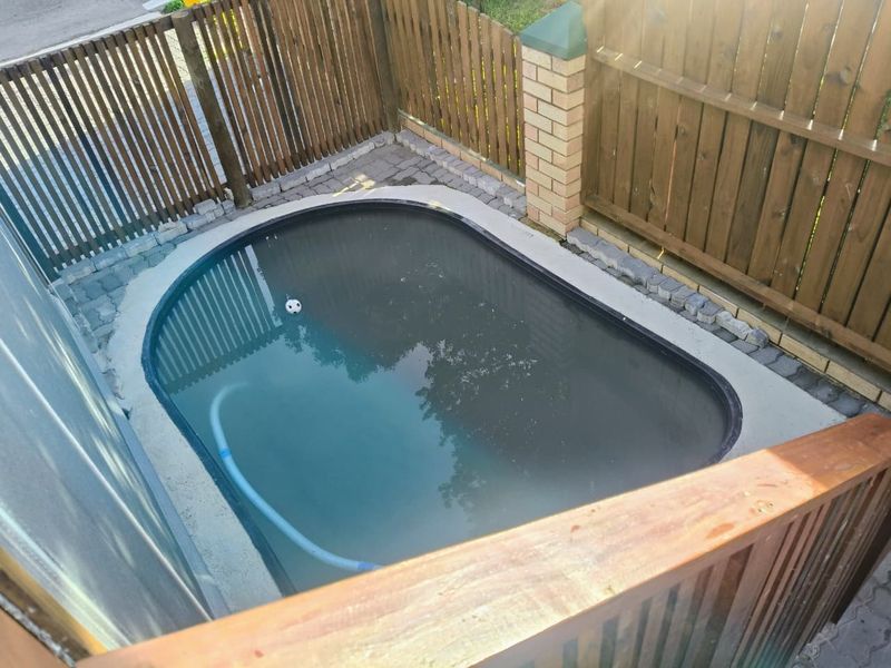 A compact plunge pool area featuring a paved surround, enclosed by timber fencing and a brick pillar.