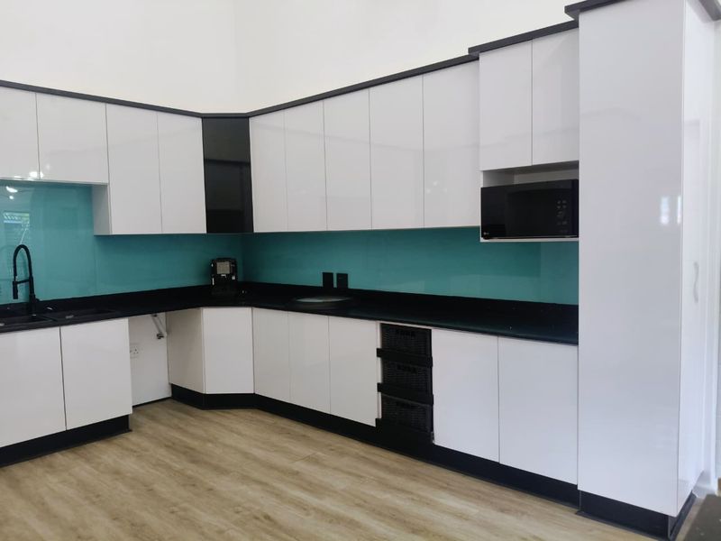Modern kitchen featuring high-gloss white cabinetry, contrasting black stone countertops, a vibrant teal glass splashback, and integrated appliances.