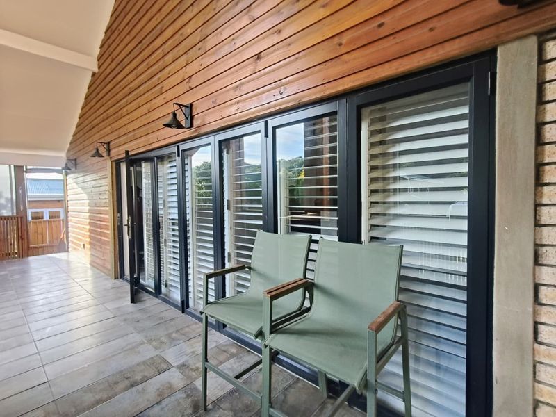 A covered patio area featuring timber wall cladding, tiled flooring, and modern black-framed bi-fold doors with integrated shutters.