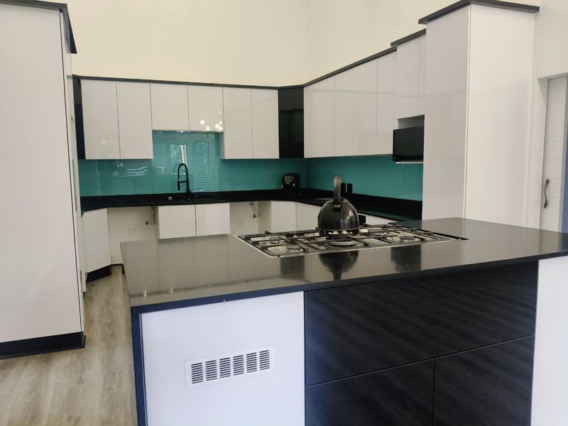 Modern kitchen featuring high-gloss cabinetry, black stone countertops, a central island with a built-in gas hob, and a vibrant glass splashback.