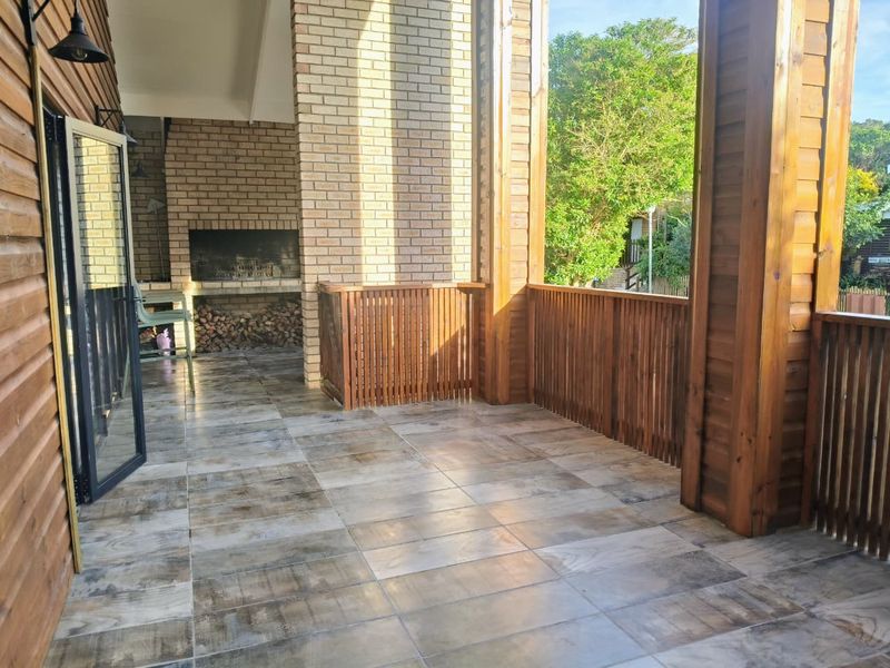 A spacious covered patio featuring tiled flooring, a built-in braai, and timber balustrades, offering a functional outdoor entertainment area.