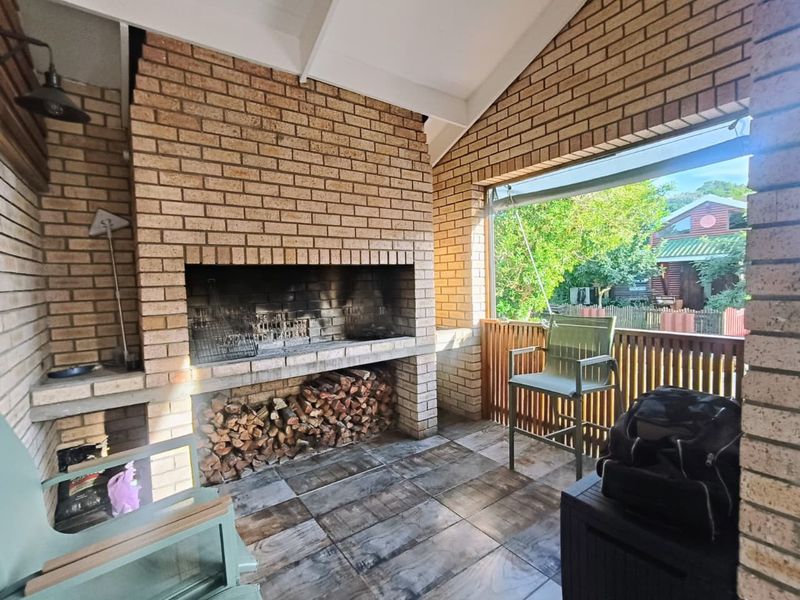 Covered patio area featuring a large built-in brick braai, tiled flooring, and timber balustrade overlooking the garden.