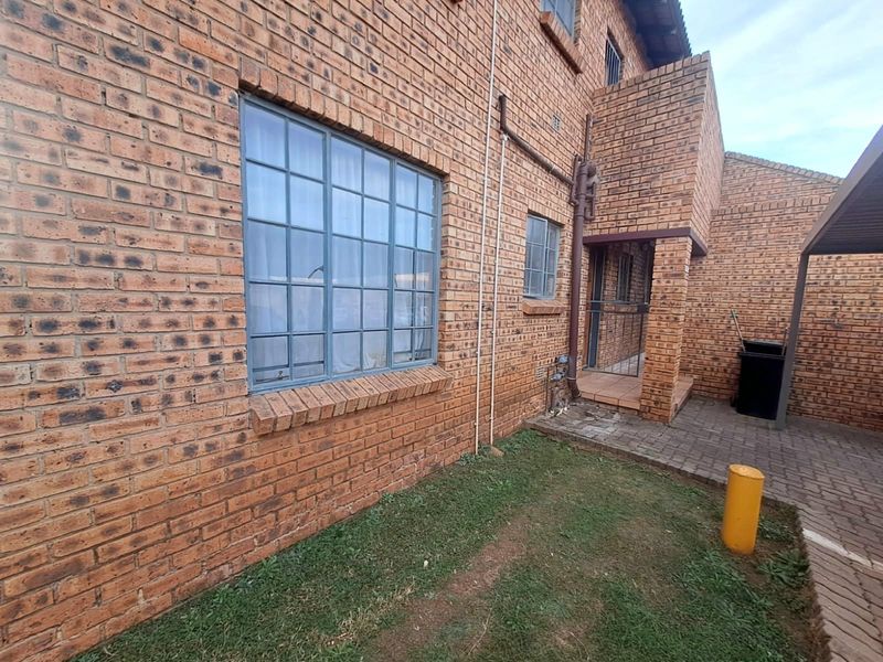 Rear exterior view of a face brick townhouse featuring a paved patio area, steel-framed windows, and functional drainage downpipes.