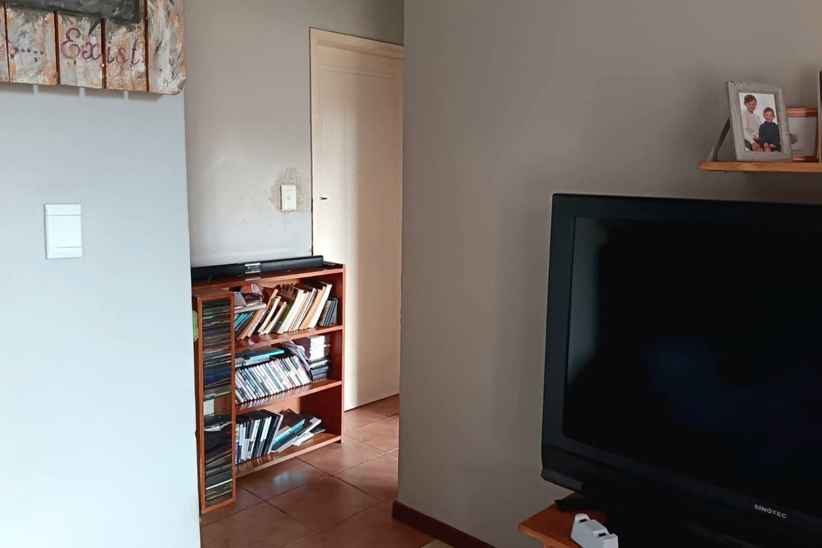 A view of a living area featuring tiled flooring and a doorway leading to an adjacent room, with visible wall surface wear.