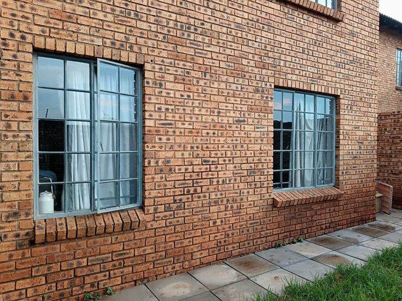 Rear exterior view of the townhouse featuring face brick walls, steel-framed windows, and a paved walkway.