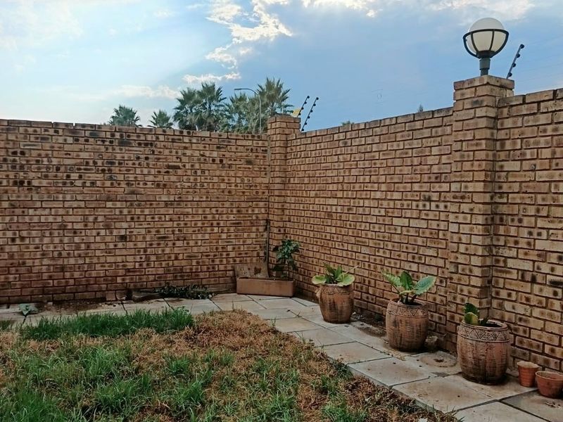 A private garden area featuring a face brick boundary wall, electric fencing, and paved walkway with established lawn.