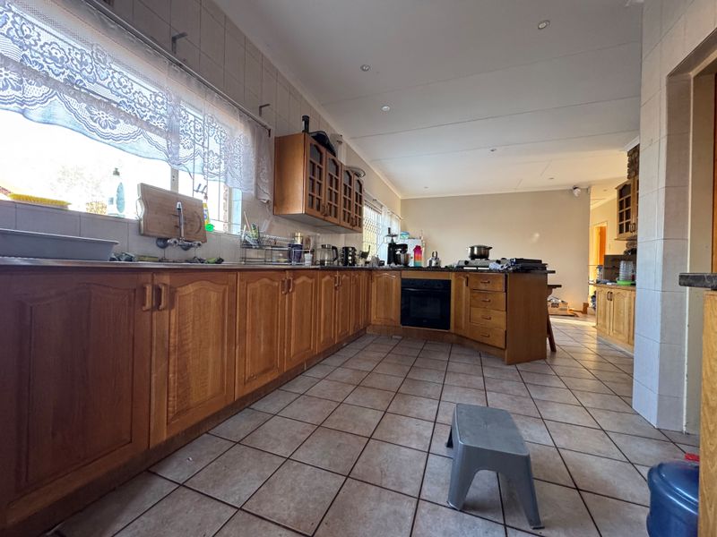 Spacious kitchen featuring extensive wooden cabinetry, built-in oven, tiled flooring, and a tiled backsplash, offering a functional layout with potential for modern updates.