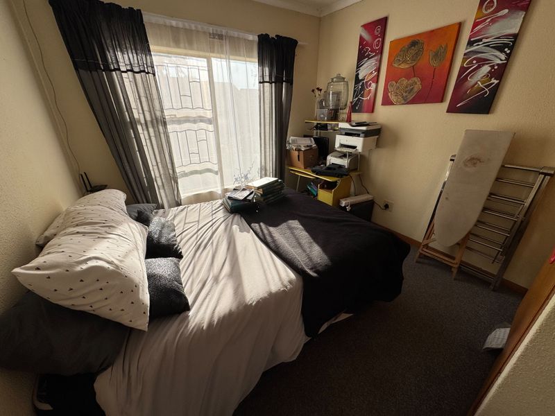 A standard bedroom featuring carpeted flooring and a sliding window fitted with security bars, providing natural light to the space.