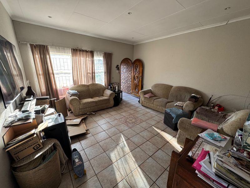 A living room featuring tiled flooring, recessed lighting, and an arched wooden entrance door, currently requiring cosmetic updates and maintenance.