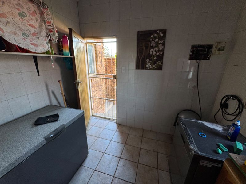 A functional laundry area featuring tiled walls and flooring, with direct access to an exterior space via a security gate.