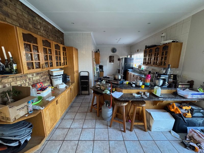 A spacious kitchen featuring wooden cabinetry, a breakfast bar, tiled flooring, and an exposed brick feature wall, offering significant potential for modernization.