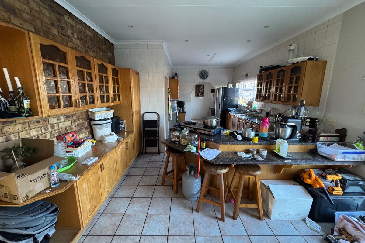 A spacious kitchen featuring wooden cabinetry, a breakfast bar, tiled flooring, and an exposed brick feature wall, offering significant potential for modernization.