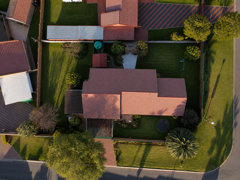 Aerial view of the property showcasing the roof structure, paved driveway, expansive lawn, and established garden areas within the fenced perimeter.