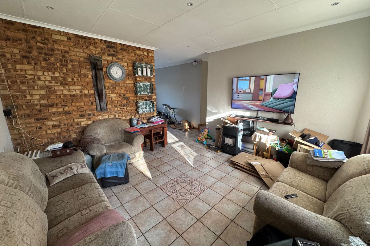 A living room featuring an exposed brick accent wall, tiled flooring, and recessed lighting, offering a functional space for relaxation.
