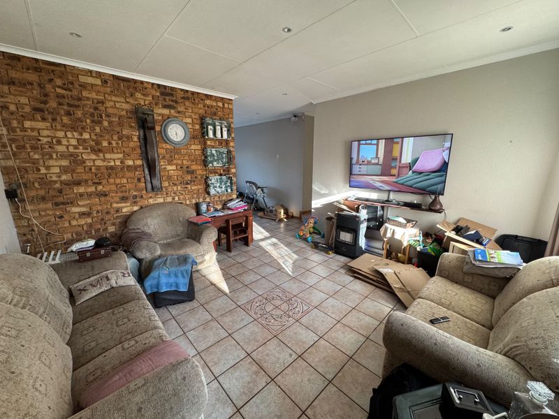 A living room featuring an exposed brick accent wall, tiled flooring, and recessed lighting, offering a functional space for relaxation.