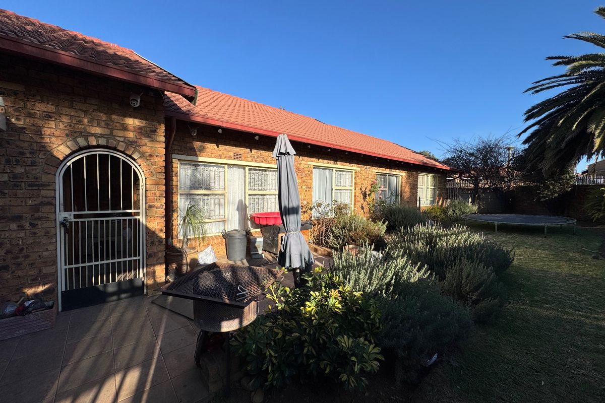 Rear view of the house featuring a face brick facade, tiled roof, paved patio area, and established garden.