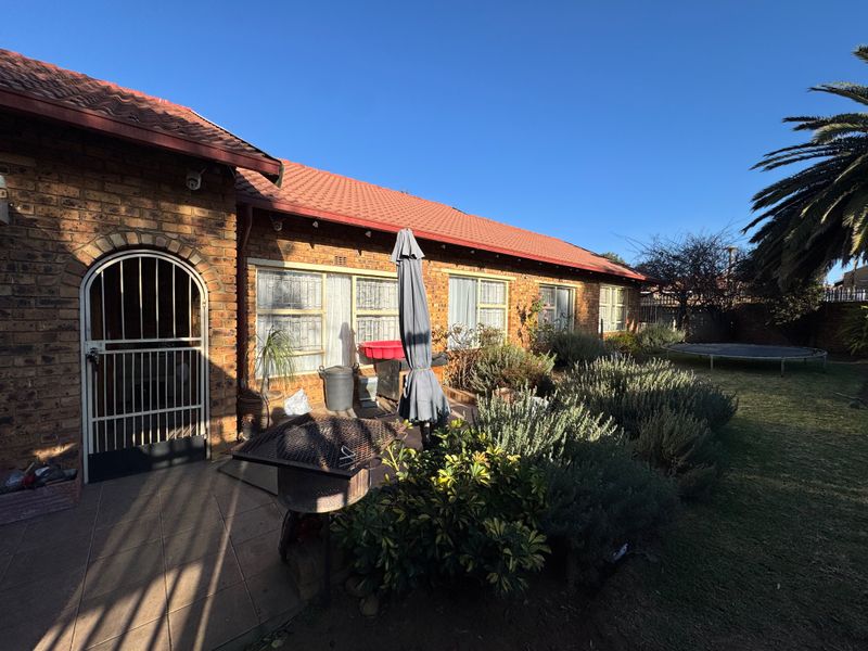 Rear view of the house featuring a face brick facade, tiled roof, paved patio area, and established garden.