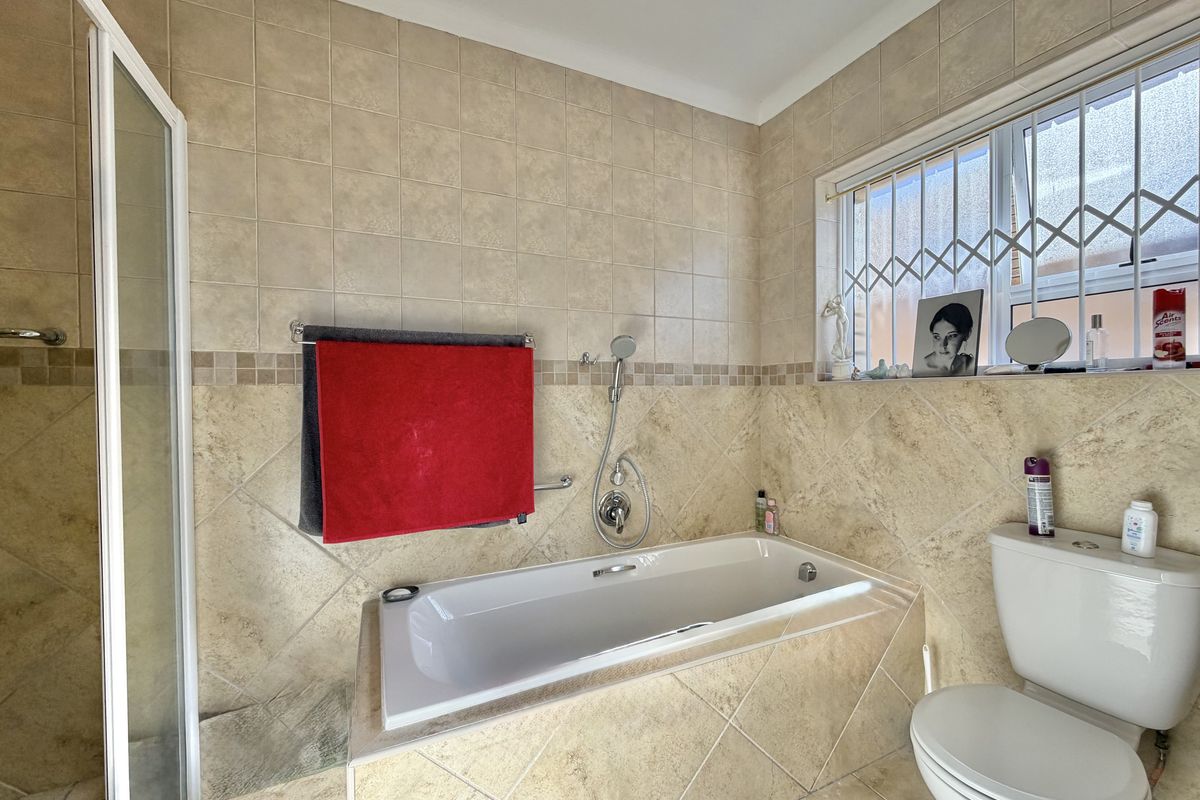 A functional bathroom featuring a built-in bathtub, separate shower enclosure, and toilet, finished with neutral ceramic wall and floor tiling.