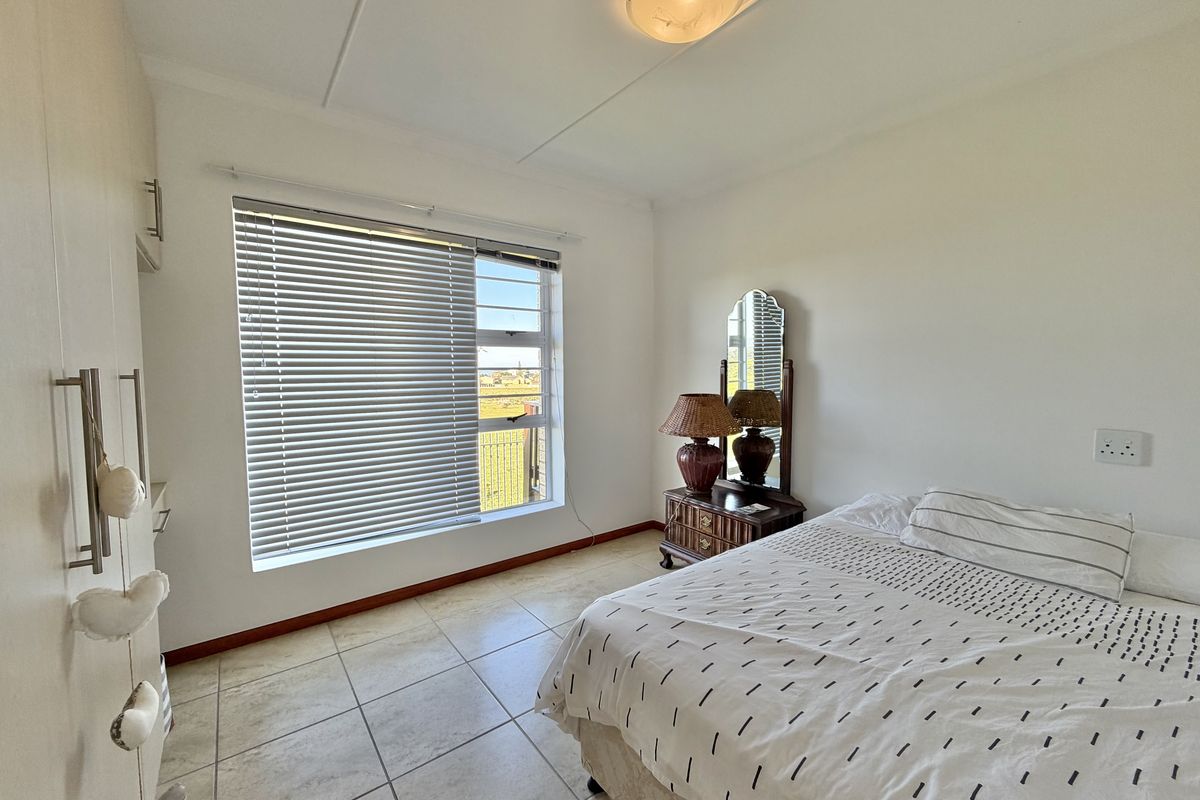 A functional bedroom featuring tiled flooring, built-in cupboards, and a large window with venetian blinds, offering a bright and practical living space.