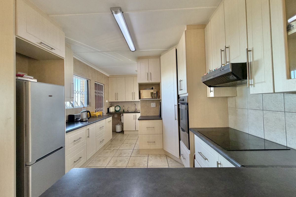 A functional kitchen featuring light-toned cabinetry, dark countertops, built-in oven, electric hob, extractor fan, and tiled flooring.